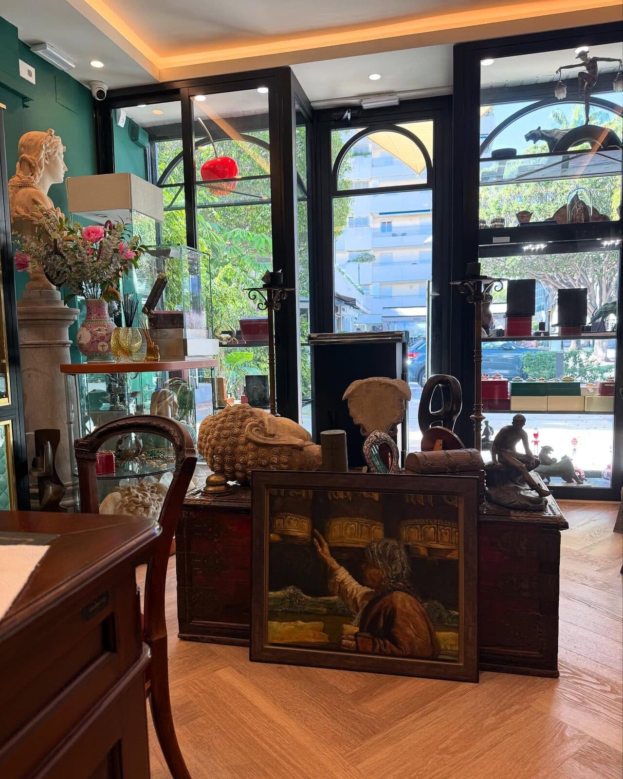 Inside the Puerto Banus shop: glass cabinets, antiques and a painting on a herringbone floor.