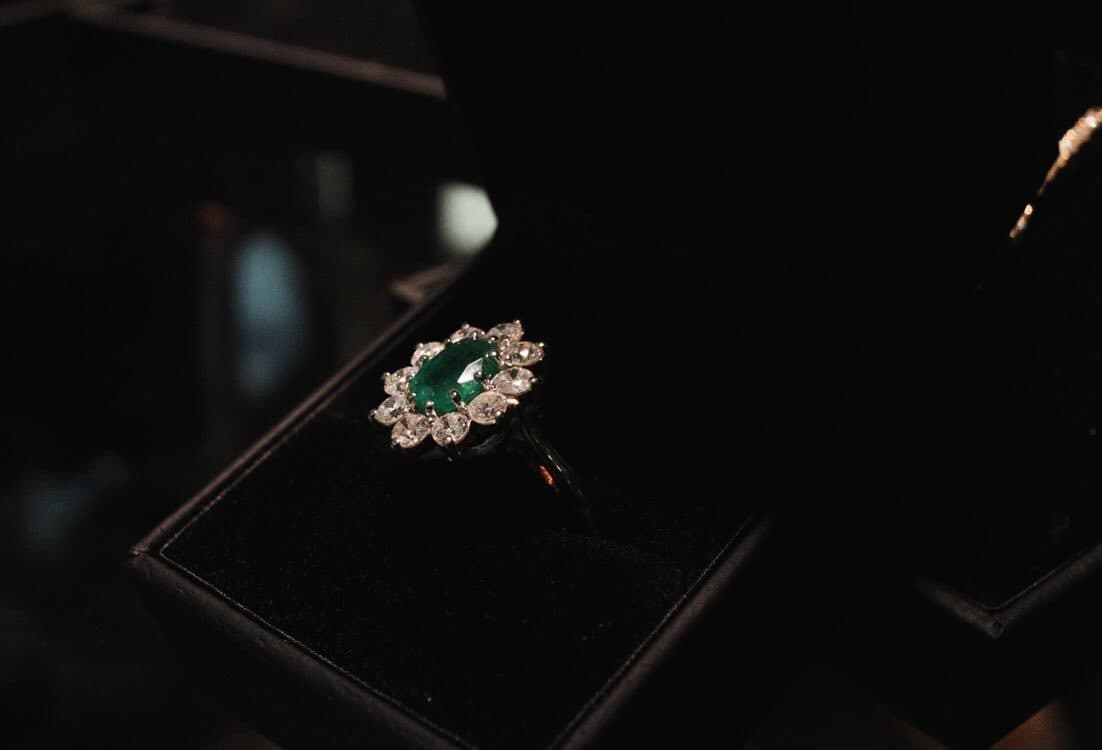 A ring with a green stone in an open black box, lit against the dark.