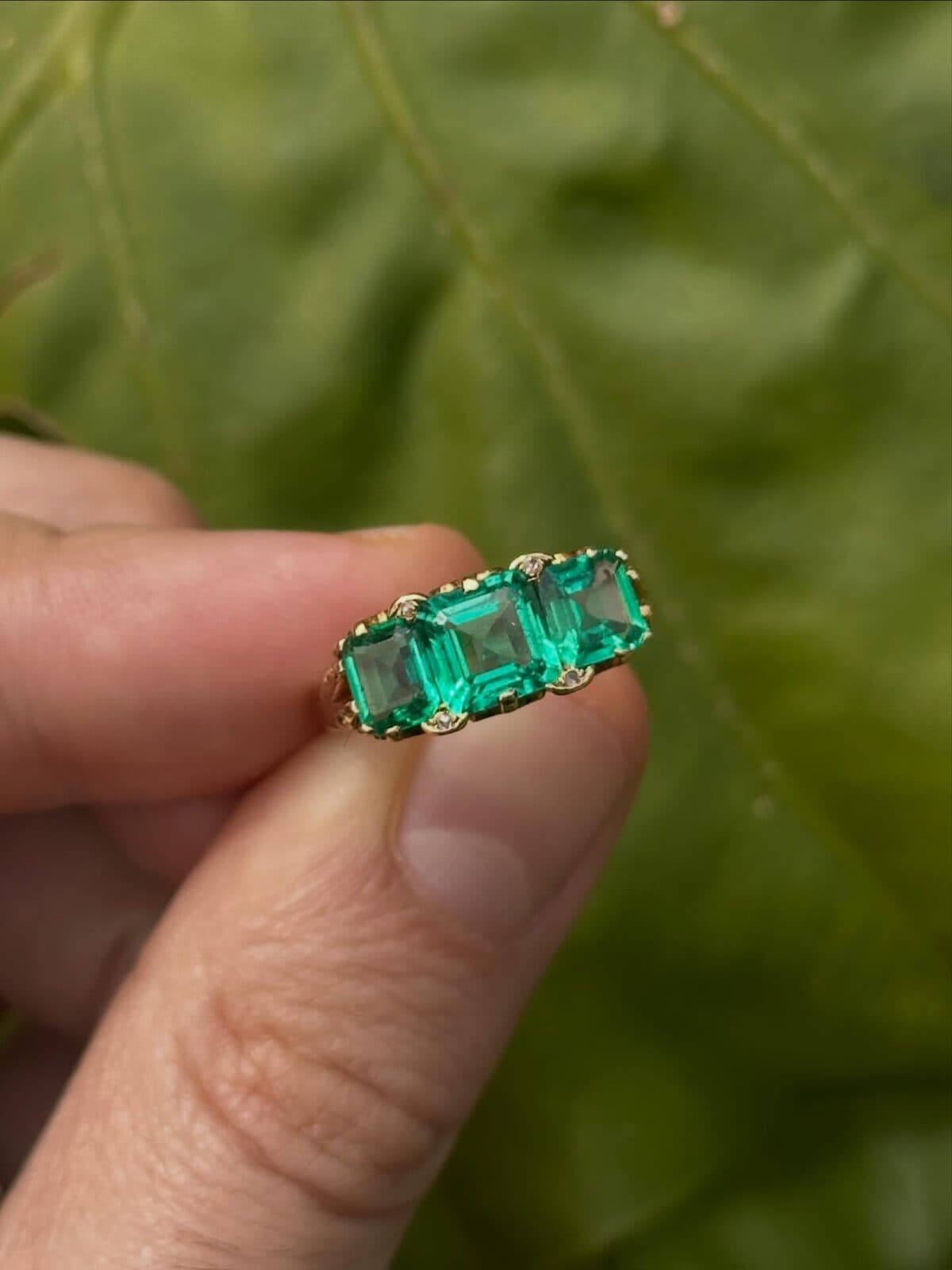 A ring with three green stones held between finger and thumb.