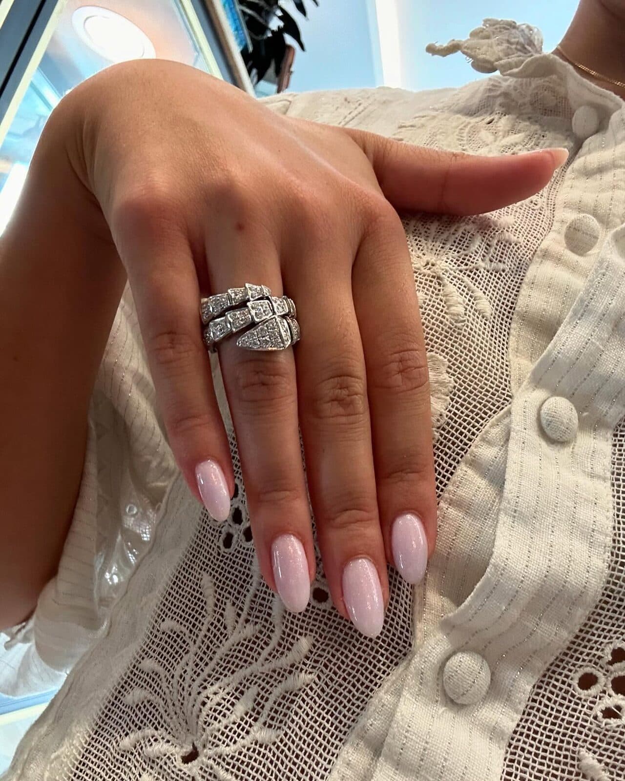 A hand wearing a wide ring, resting on white lace.
